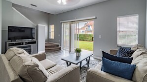 A living room with a TV, sofa, coffee table, and a view of the outside.