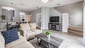 A modern living room with a sofa, coffee table, and TV. There is a staircase leading to another level.