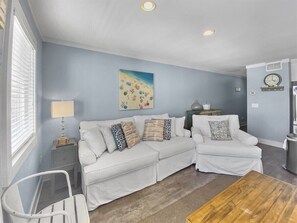 A living room with a white sofa set, a coffee table, a lamp, and a painting on the wall. - Quaint Gulf Front Condo | Leeward II Unit 5 | Seag (Santa Rosa Beach)