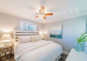 A bedroom with a bed, a ceiling fan, a window with blinds, a bedside lamp, and a painting on the wall. - Quaint Gulf Front Condo | Leeward II Unit 5 | Seag (Santa Rosa Beach)