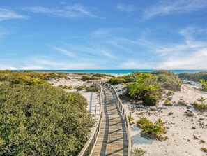A wooden boardwalk leading to a beach with dunes and sparse vegetation.