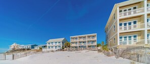 A beachfront hotel with multiple-story buildings, a sandy beach, and a clear blue sky.