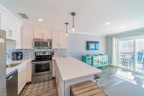 A modern kitchen with stainless steel appliances, a large island, and a view to the outside. - Quaint Gulf Front Condo | Leeward II Unit 5 | Seag (Santa Rosa Beach)