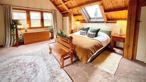 Un dormitorio acogedor con techo inclinado, muebles de madera, una cama grande, un banco y vistas al exterior a través de una ventana.