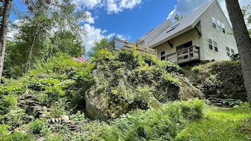 Una casa con una scala in pietra che conduce a un terrazzo in legno, immersa nel verde e alberi.