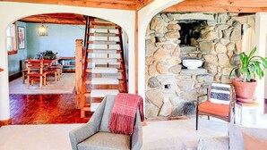 Un interior rústico con chimenea de piedra, escalera de madera y una zona de estar acogedora.