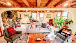 Una sala de estar acogedora con chimenea de piedra, vigas de madera en el techo y un espacio de descanso cómodo con sofá y sillones.
