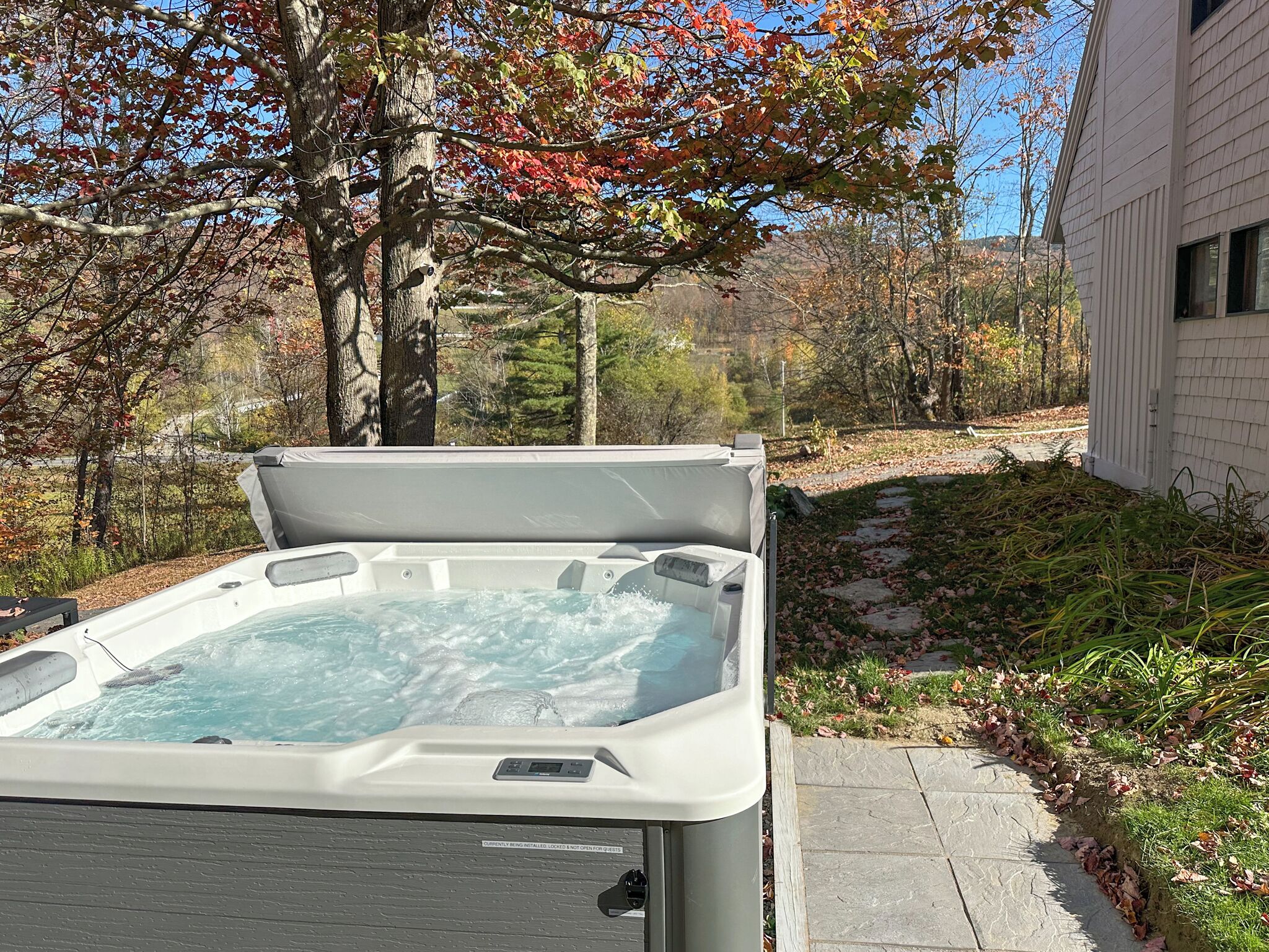 Un bain à remous dans un jardin, avec un chemin de pierres et des arbres.