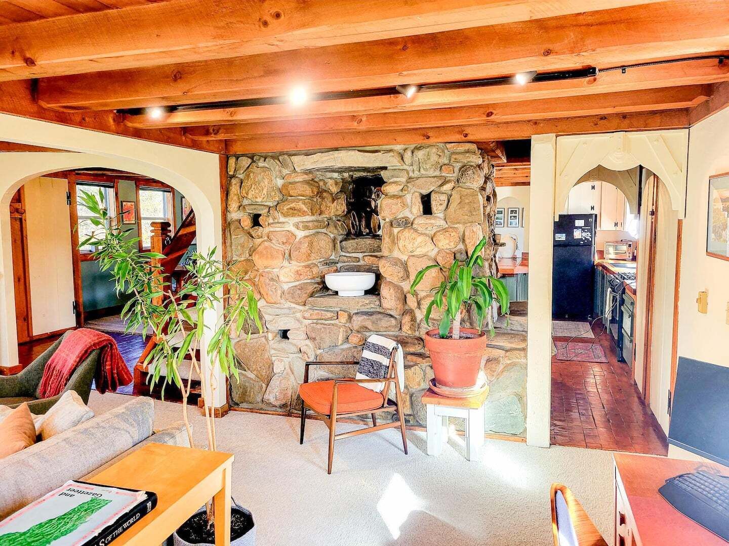 A cozy living area with a stone fireplace, wooden beams, and a view into the kitchen.