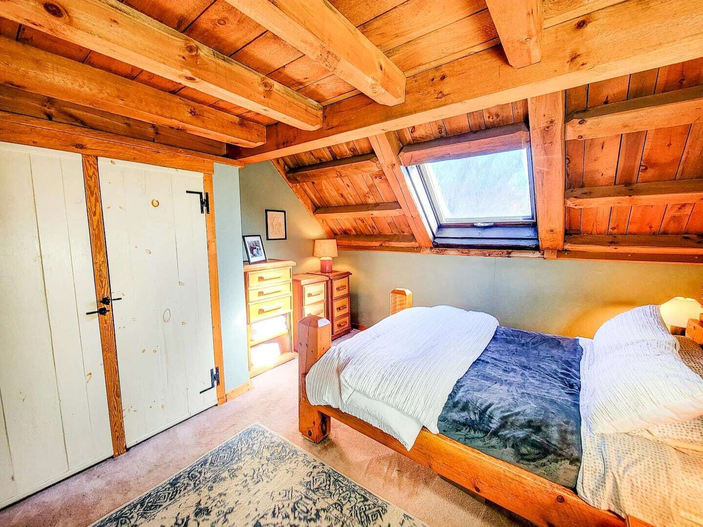Een slaapkamer met twee bedden, houten balken in het plafond, een dakraam, een kledingkast en een bureau met lades.