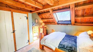 Een slaapkamer met twee bedden, houten balken in het plafond, een dakraam, een kledingkast en een bureau met lades.