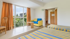 A hotel room with a large window, a yellow sofa, a striped bed, and a wooden chair. - Hotel Gloria - All Inclusive (Varna)