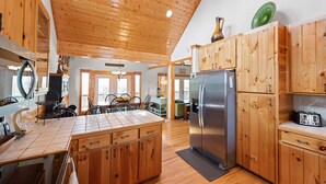 A kitchen with wooden cabinets, a stainless steel refrigerator, and a tiled island. - Sweeping Mountain Views | Wraparound Decks | Cloud Rise (Piney Creek)