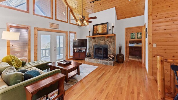 A spacious living room with a stone fireplace, wooden ceiling, and large windows. - Sweeping Mountain Views | Wraparound Decks | Cloud Rise (Piney Creek)