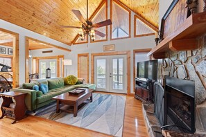 A spacious living room with a wooden ceiling, a fireplace, a green sofa, and a stone wall.