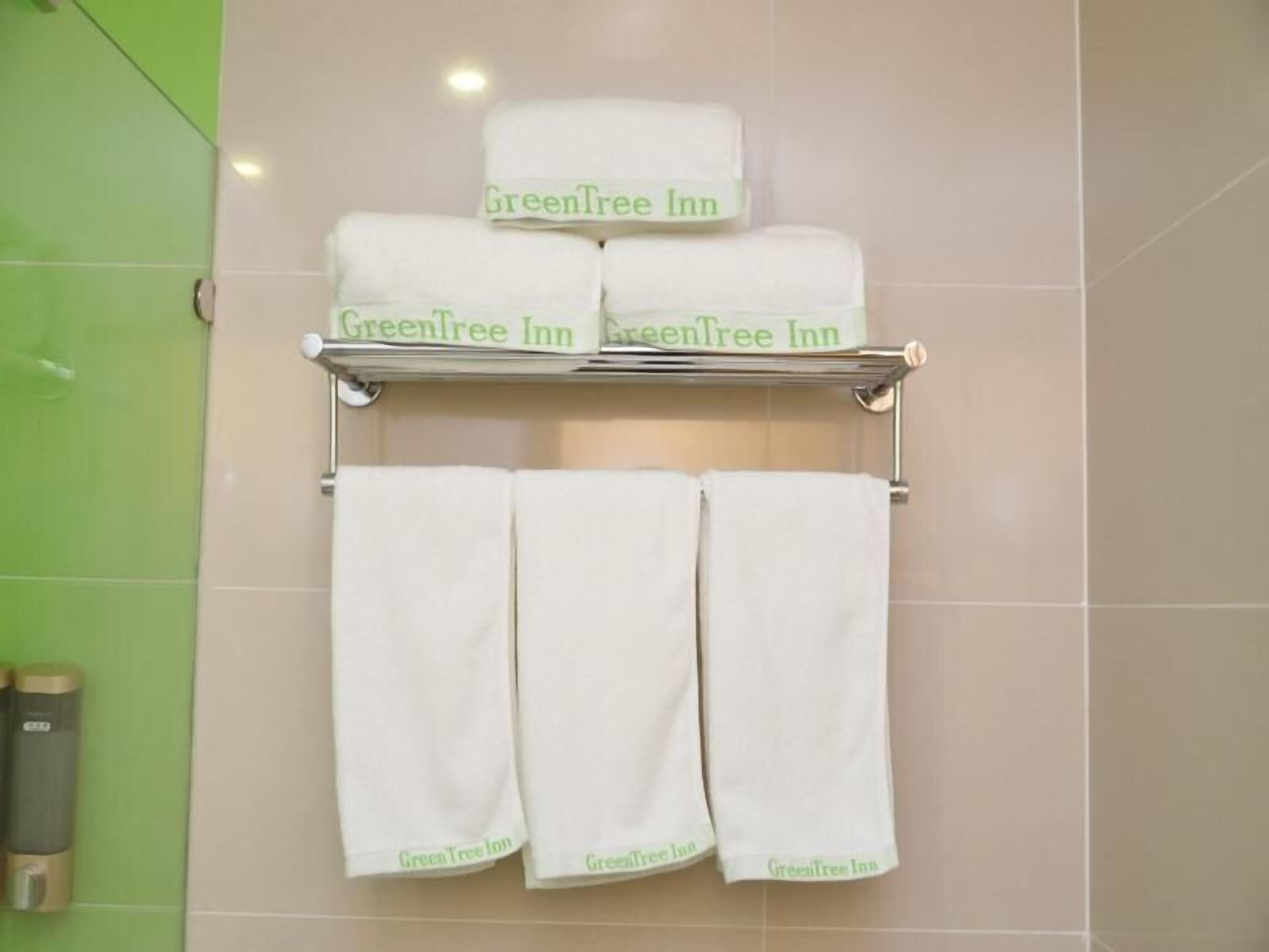Ein Badezimmer mit einem Handtuchhalter, der drei weiße Handtücher und ein gefaltetes Handtuch trägt. Die Wand ist mit grünen Fliesen und einem beigefarbenen Handtuchhalter versehen.