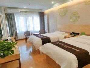 Habitación de hotel con dos camas, un escritorio con silla, una planta en maceta y una ventana con cortinas.