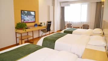 A hotel room with three beds, a desk with a television, a chair, and a window with curtains.