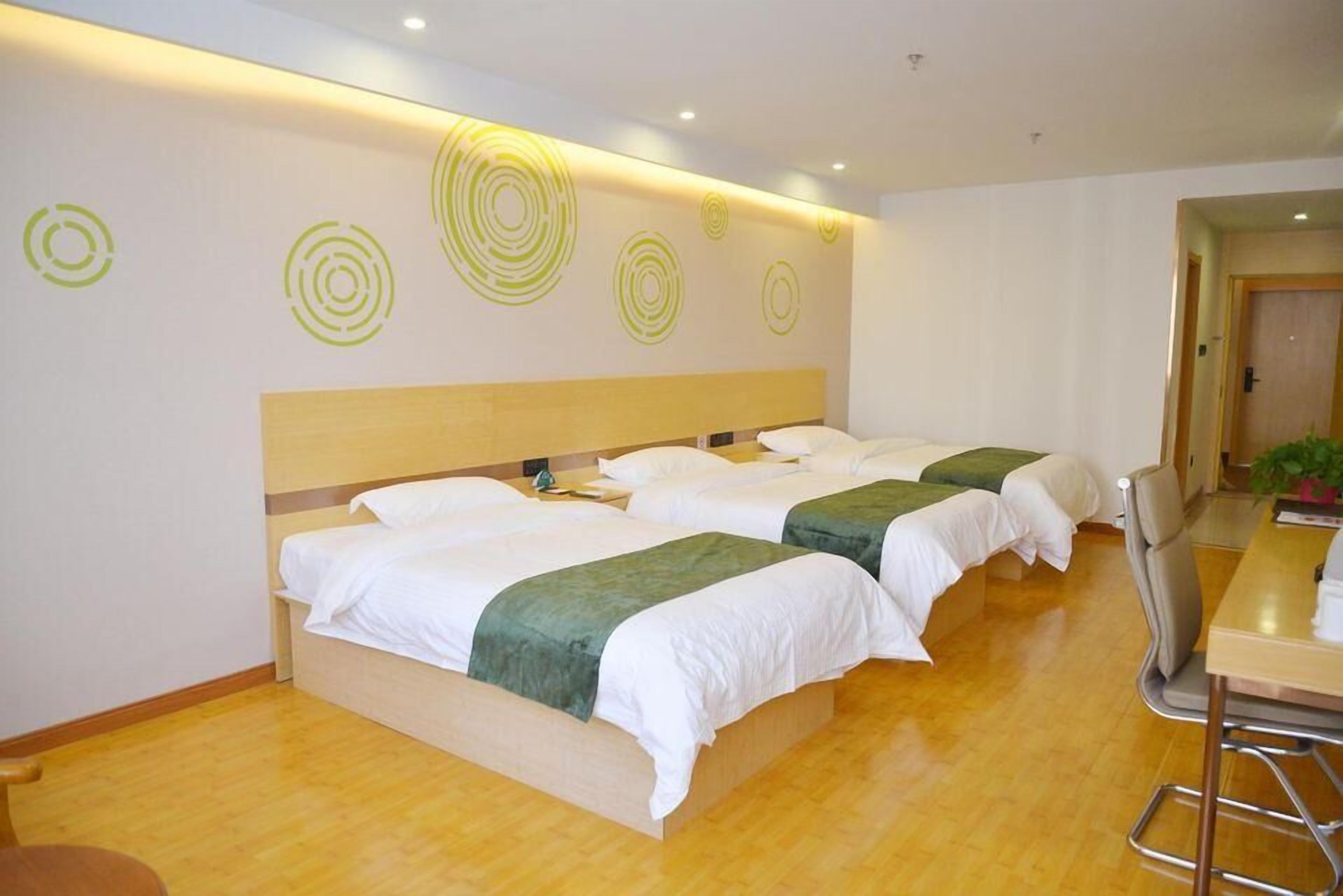 Une chambre d’hôtel avec deux lits, un plancher en bois, un bureau avec une chaise et un mur orné de motifs circulaires.