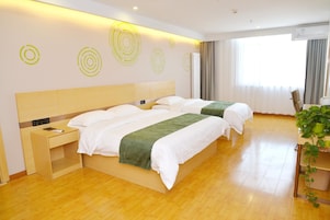 Quarto de hotel com duas camas, mesa de cabeceira, planta em vaso e janela com cortinas.