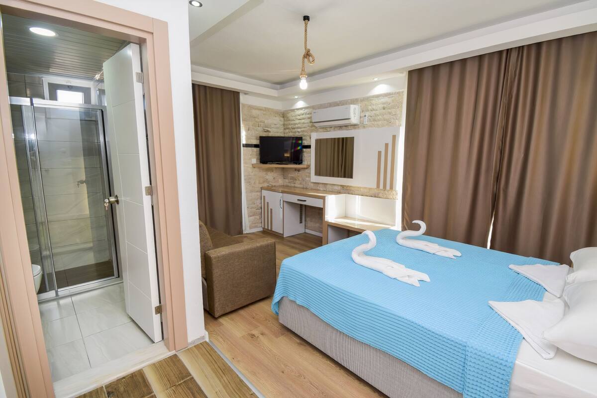 Een hotelkamer met een douche, een bed met een blauwe sprei, een bureau met een flatscreen televisie en een badkamer met een toilet.