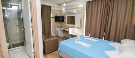A hotel room with a shower, a bed with a blue bedspread, a desk with a flat-screen TV, and a bathroom with a toilet.