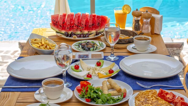 A table set with various dishes, including watermelon slices, a salad, and a plate of spring rolls, by a poolside. - Esmeralda Butik Hotel (Manavgat)