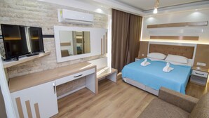 A modern hotel room with a flat-screen TV, a desk, a bed with a blue bedspread and two swan-shaped pillows, a mirror, an air conditioning unit, and a wooden floor. - Esmeralda Butik Hotel (Manavgat)