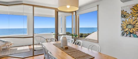 A dining area with a wooden table, white chairs, and a view of the ocean.