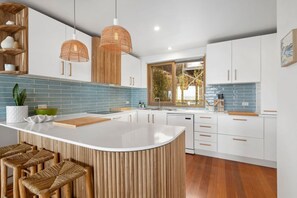A modern kitchen with a central island, wooden bar stools, and a large window.