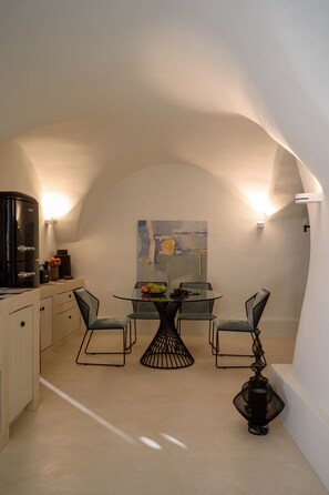 Une cuisine compacte avec une table à manger ronde, deux chaises, une machine à café et un tableau accroché au mur.