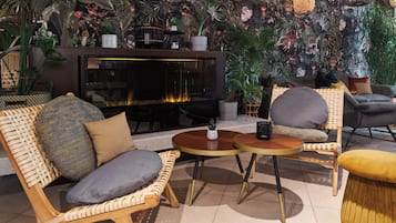 Uma área de estar acolhedora, com mobiliário de vime, lareira e decoração com plantas exuberantes.