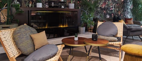A cozy lounge area with wicker furniture, a fireplace, and lush plant decorations.