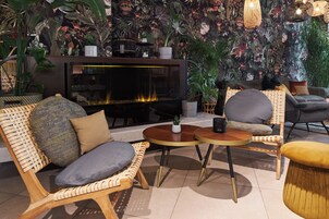 Un rincón acogedor con mobiliario de mimbre, chimenea y decoración con plantas exuberantes.