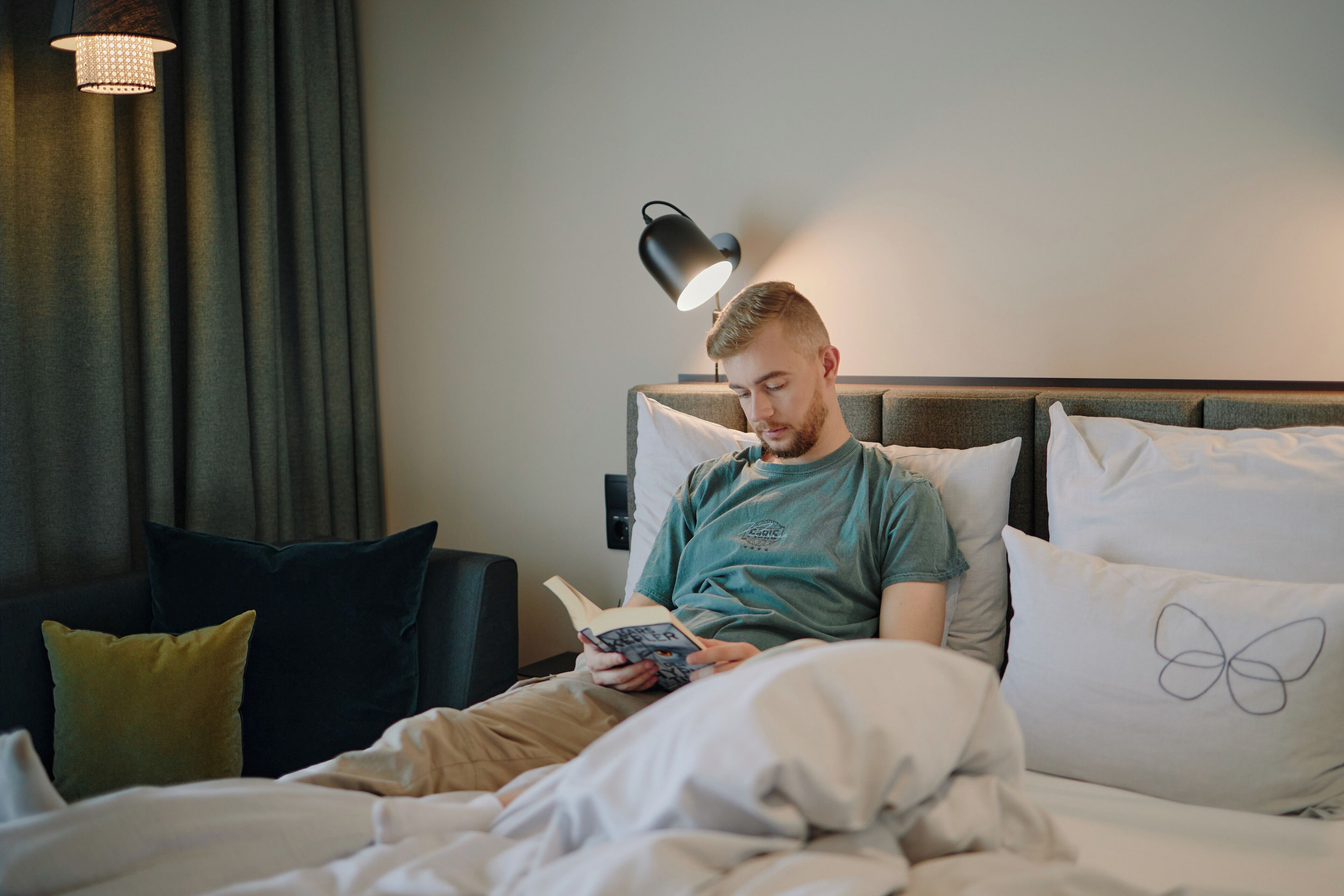 A person sitting on a bed with a book, a lamp, and a pillow with a butterfly design.
