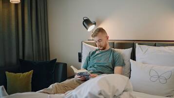 A person sitting on a bed with a book, a lamp, and a pillow with a butterfly design.