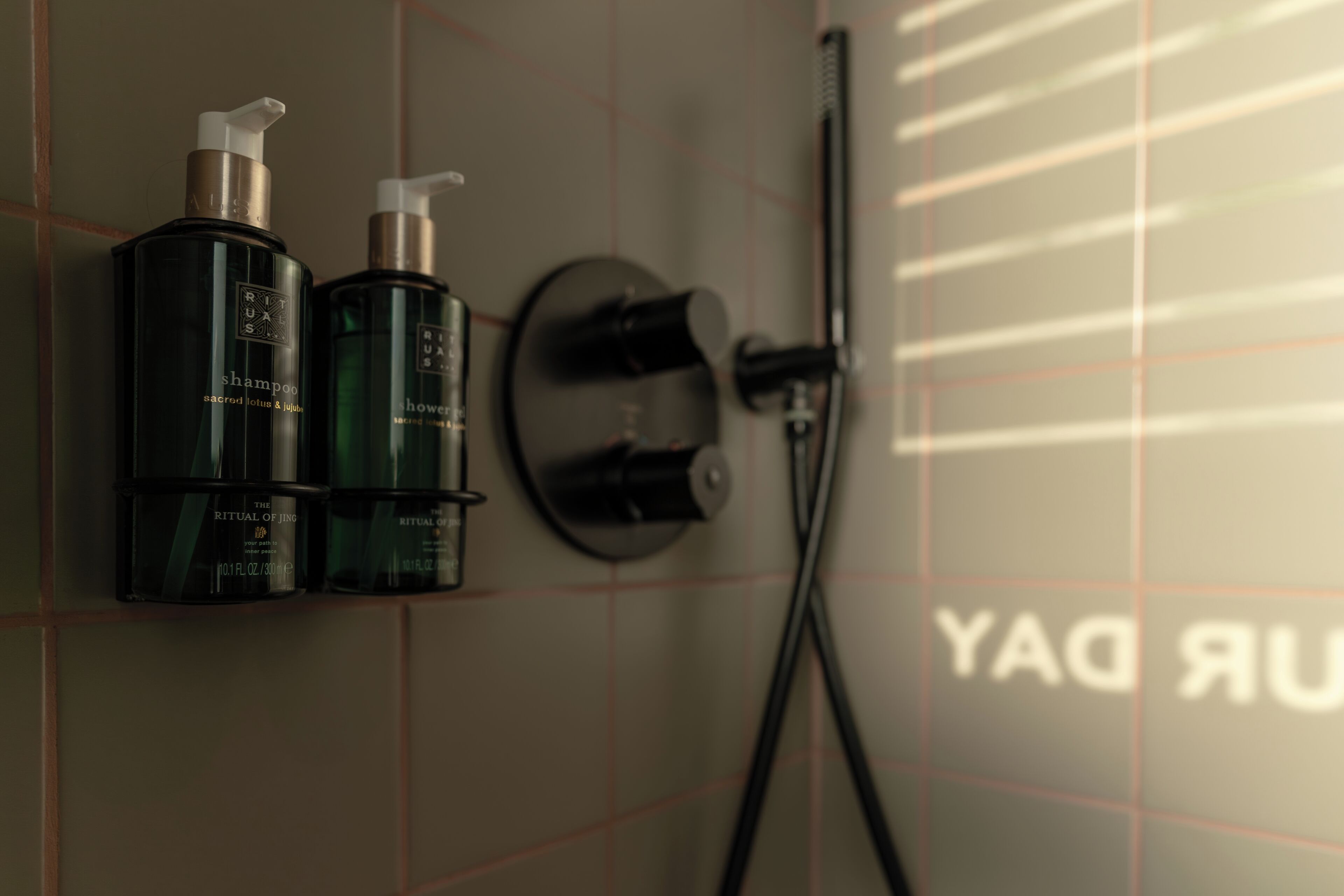 Un baño con ducha, dos botellas de champú y un perchero.