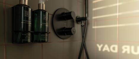 Un baño con ducha, dos botellas de champú y un perchero.
