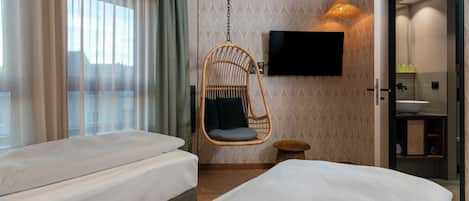 Une chambre d’hôtel avec deux lits, un fauteuil suspendu, une télévision et une salle de bain.