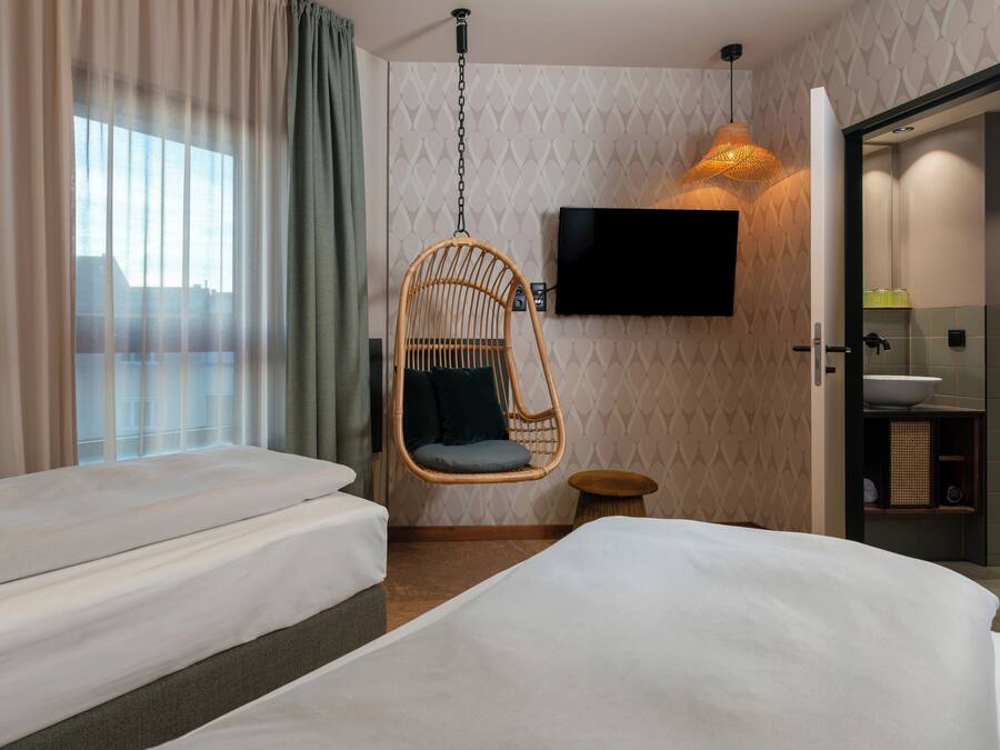 Ein Hotelzimmer mit zwei Betten, einem Hängesessel, einem Fernseher und einem Badezimmer.