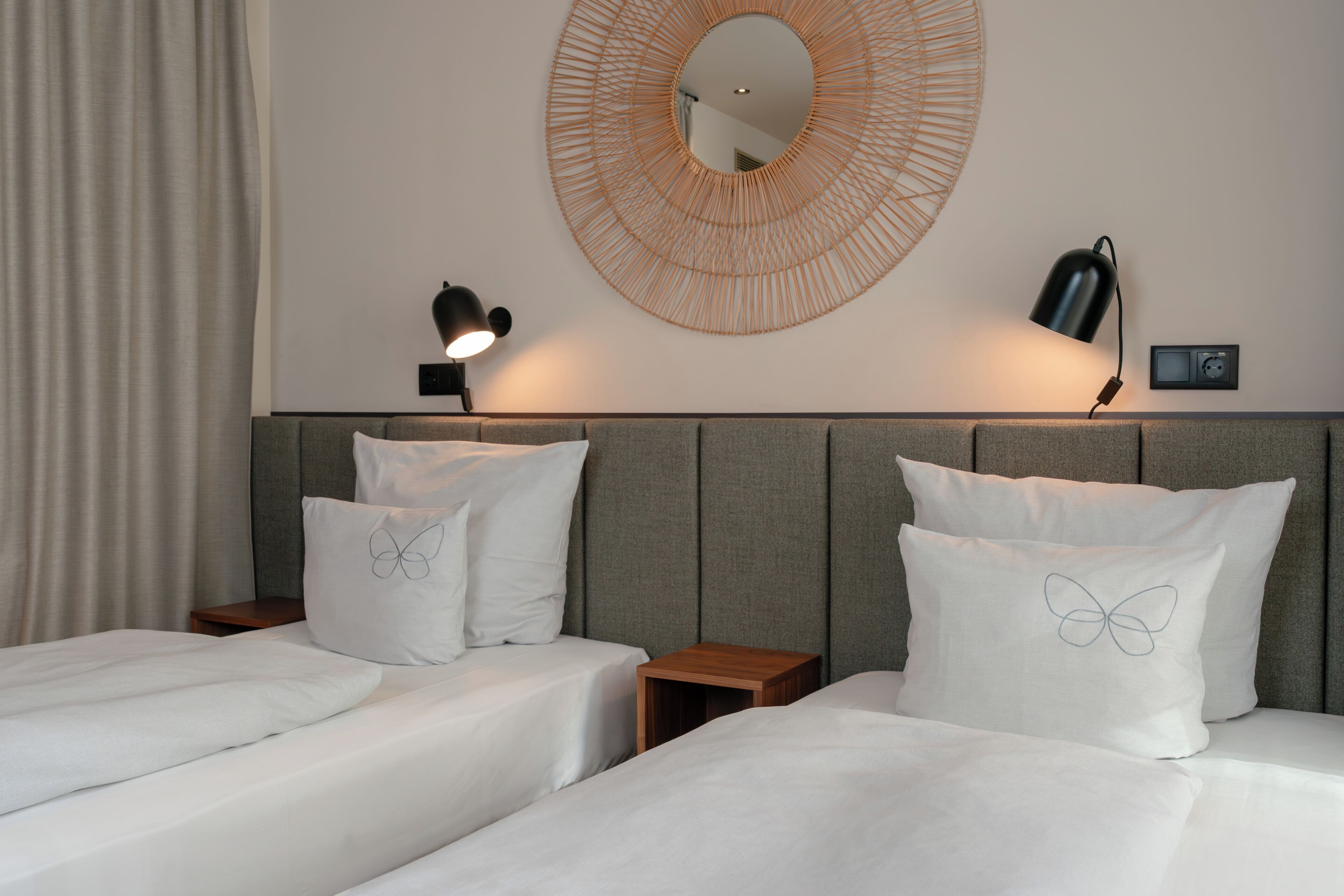 A hotel room with two beds, a round mirror, and two bedside lamps.