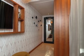 Un pasillo con piso de madera, televisor montado y pared con diseño.