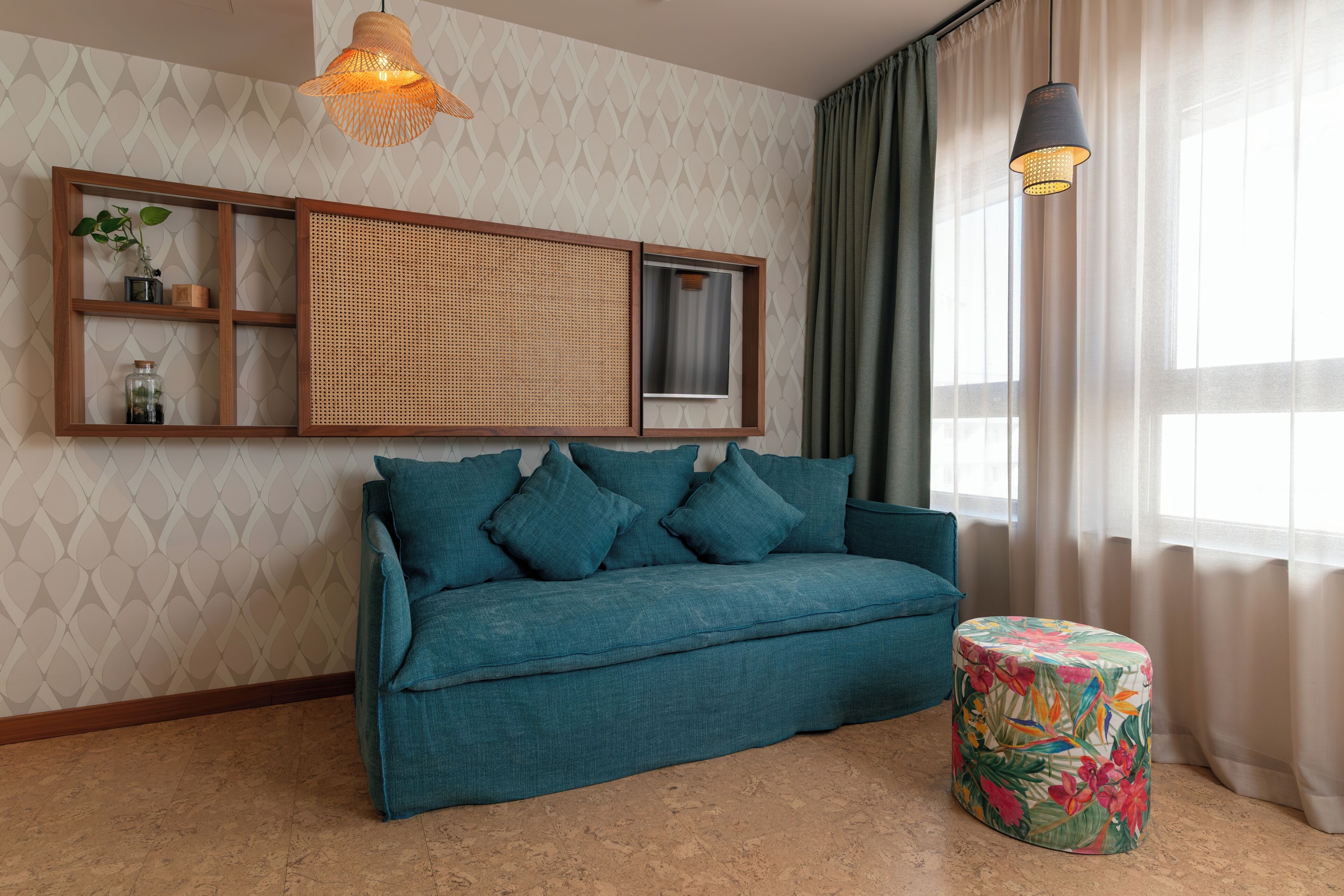 A teal sofa with cushions, a woven shelf unit, a small round ottoman with a floral cover, and two pendant lights.