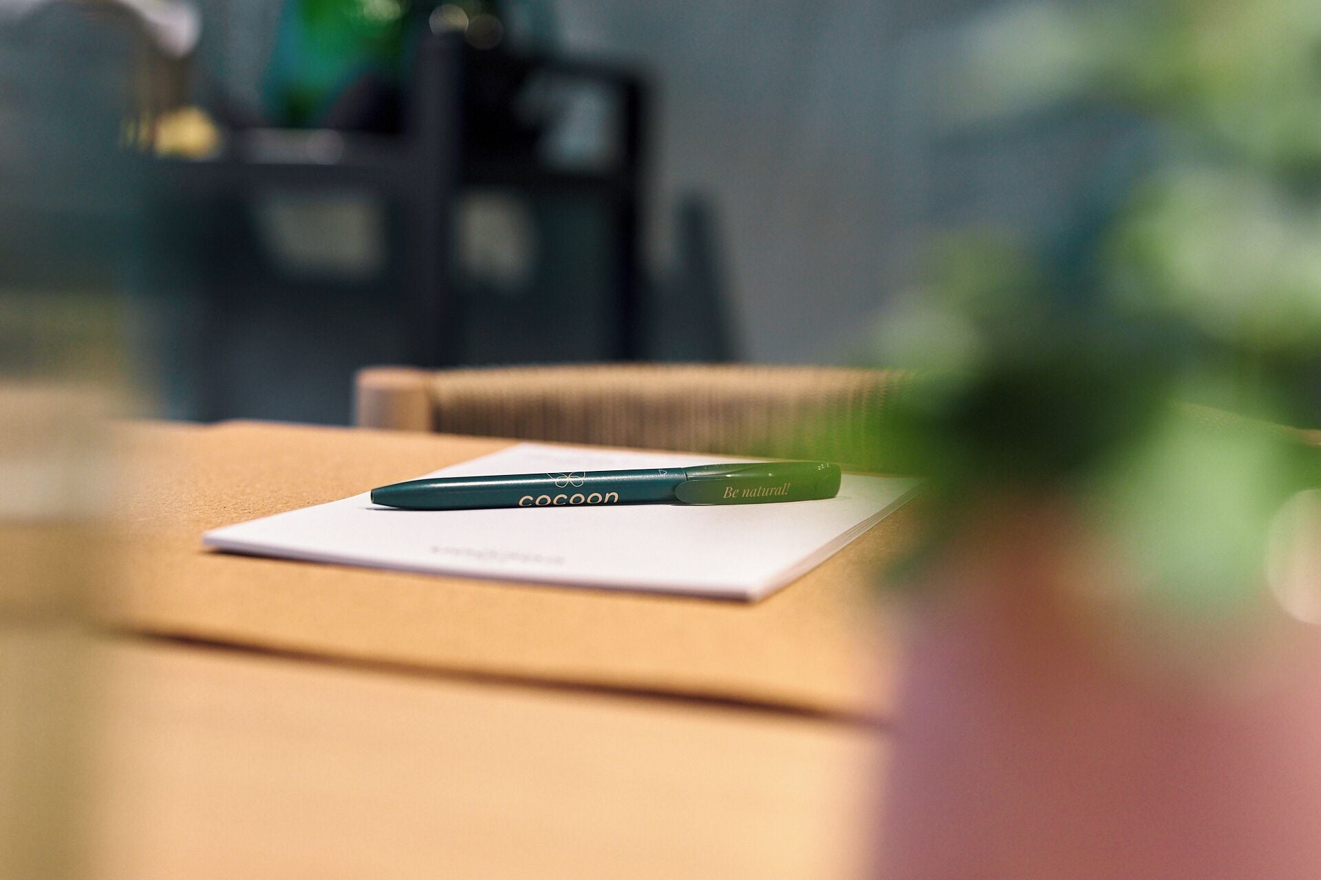 A green pen on a white paper with the text 'COCON' and 'Be natural!' on a table.