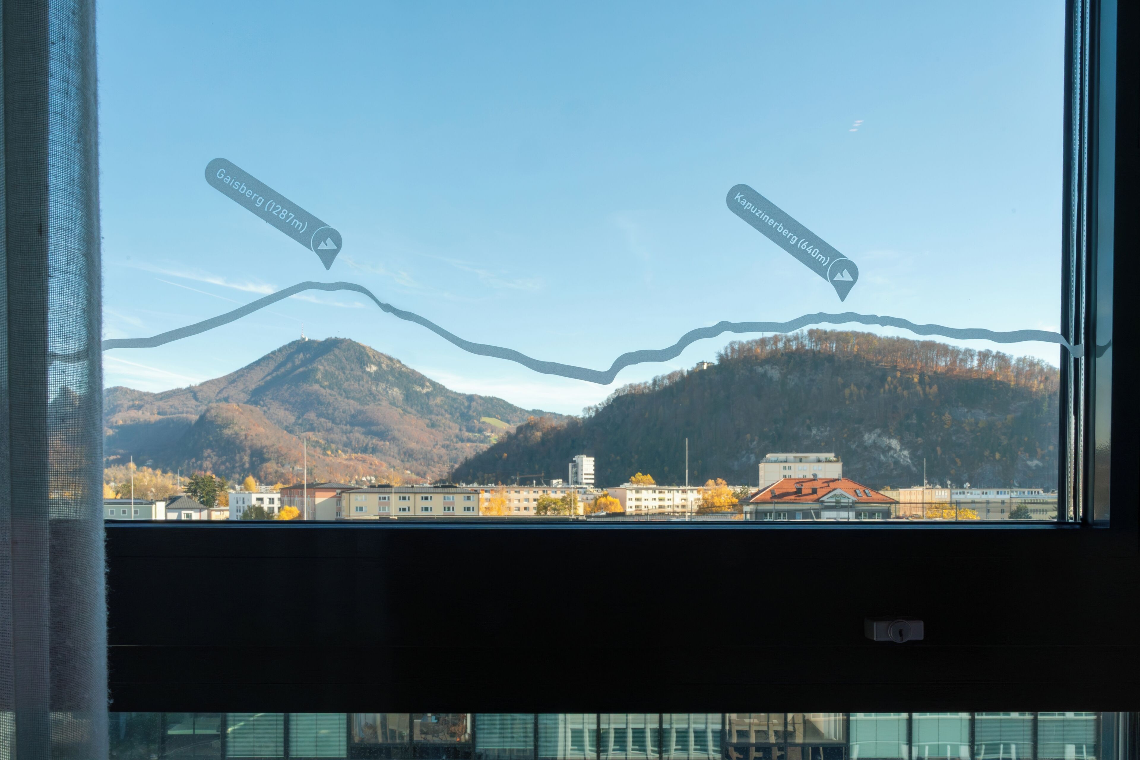 A view through a window with a mountain and buildings in the background.