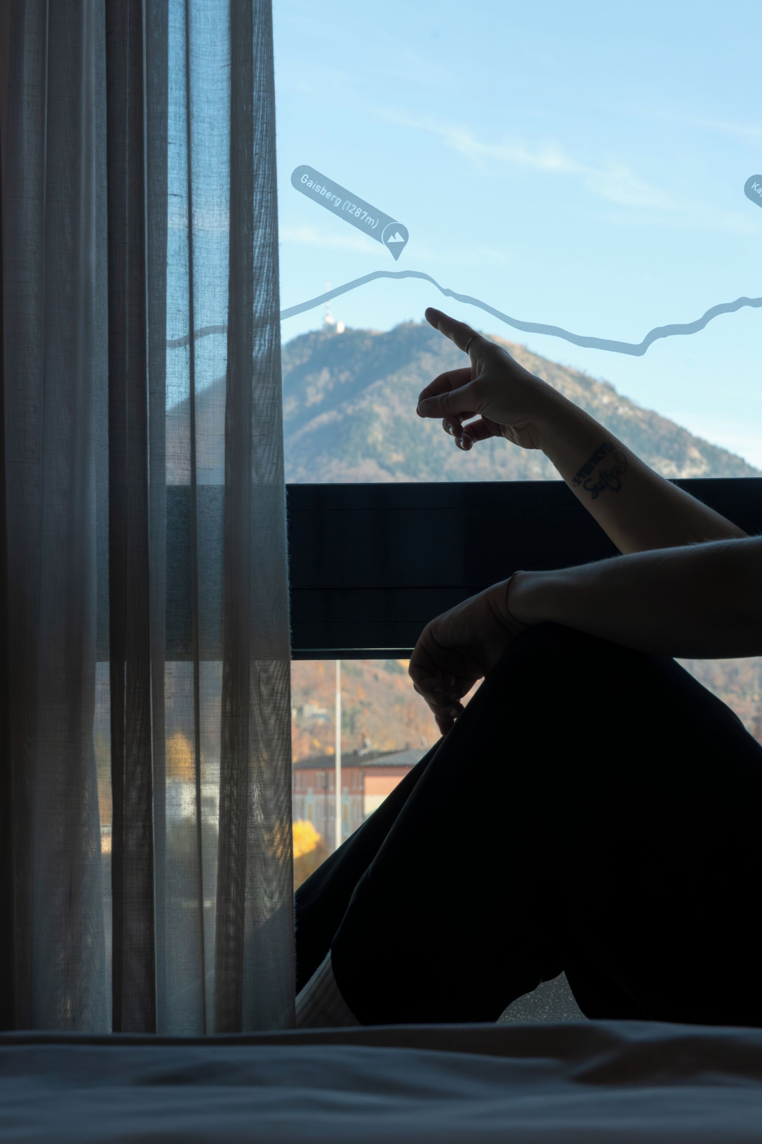 Una persona sentada junto a una ventana con vistas a una montaña y un paisaje urbano.