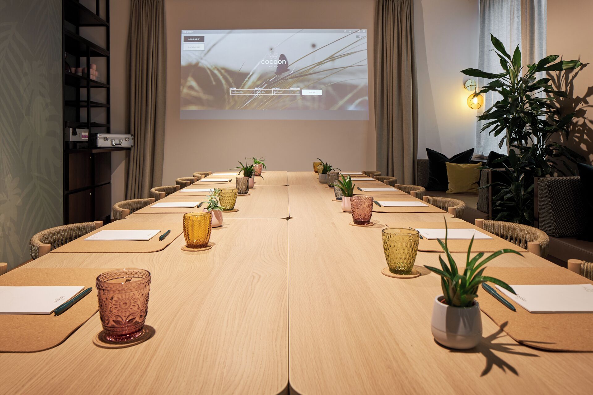 A conference room with a long table, chairs, and a screen displaying a presentation.