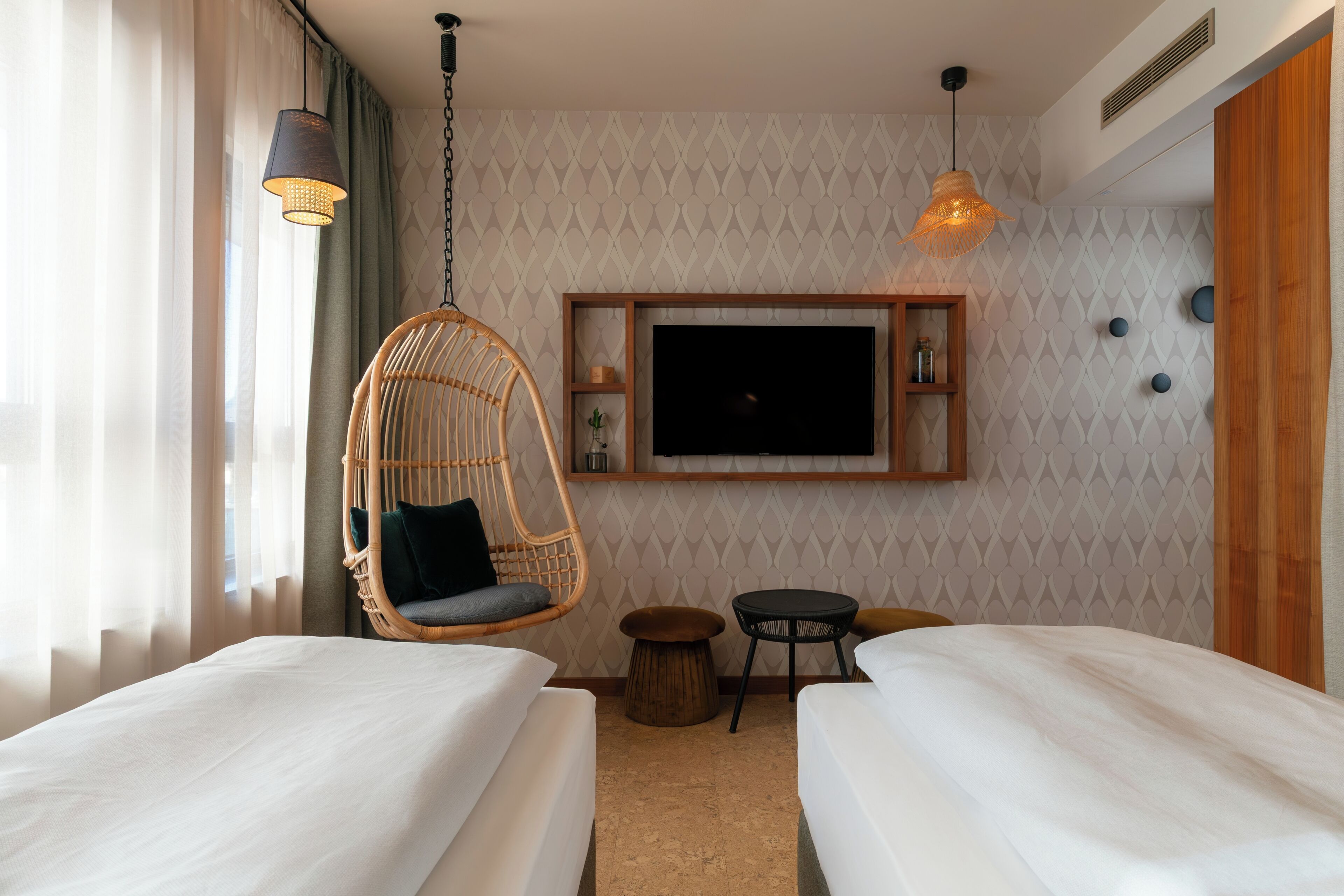 A hotel room with two beds, a hanging chair, a TV, and a small table.