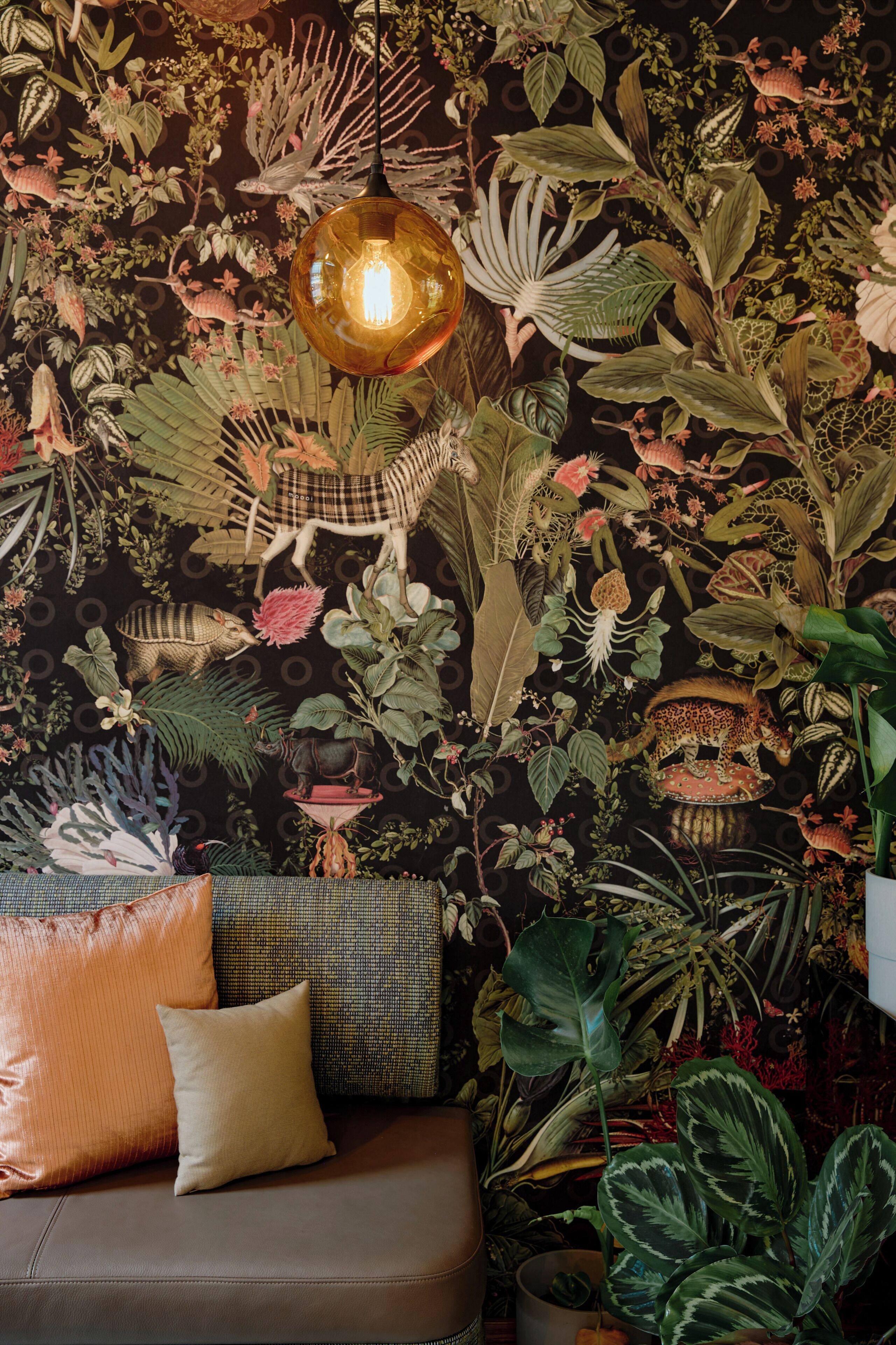 A room with a sofa, pillows, and a wall decorated with various plants and a hanging light fixture.