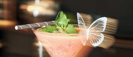 Un cóctel en una copa de martini con una decoración de mariposa sobre un posavasos.